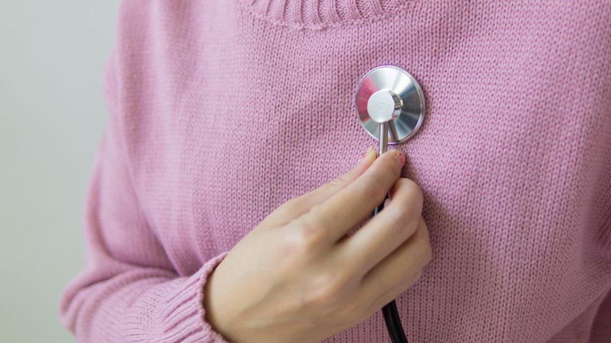 검사 전에는 무엇을 준비하고 확인하면 좋을까요? — 옷차림과 장신구, 금식 여부 검사받기 편안하고 꽉 끼지 않는 옷을 입는 것이 권장되며, 검사 부위에 따라 검사복으로 갈아입거나… · 사진: A person wearing a pink sweater holds a stethoscope to their chest for a…